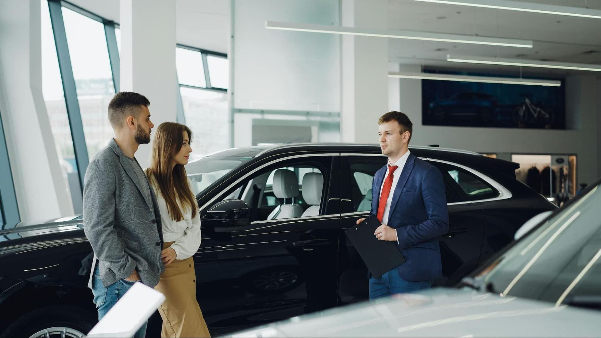 A man and a woman in a car dealership talking to a salesman