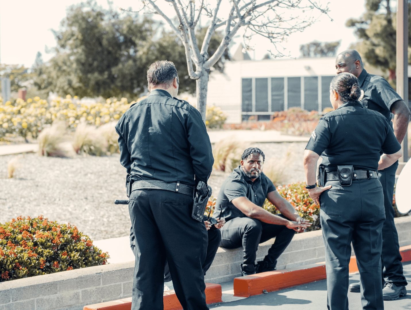 Three policemen and a policewoman gather in conversation outdoors, with one officer seated on the pavement