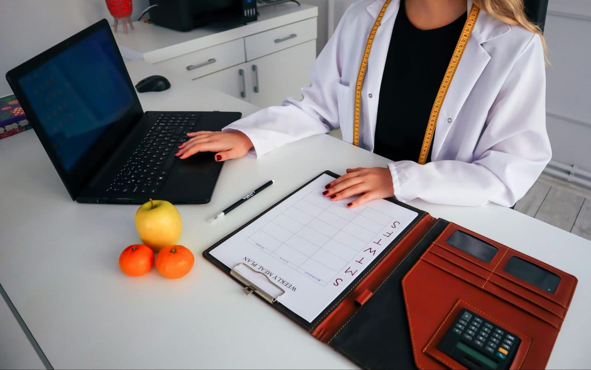 a dietitian working on a personalized nutrition plan using a laptop and a weekly calendar