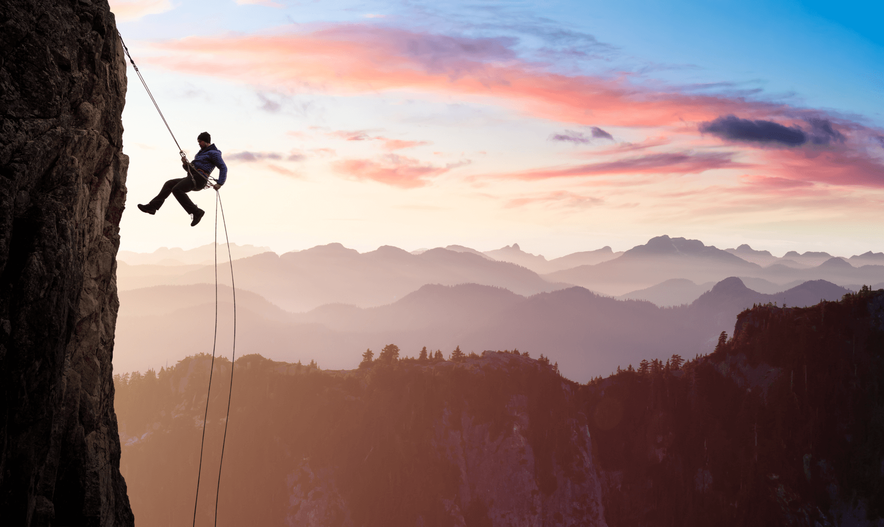 A man climbs a steep mountain using a rope, with a scenic backdrop of forested hills and a bright skyline