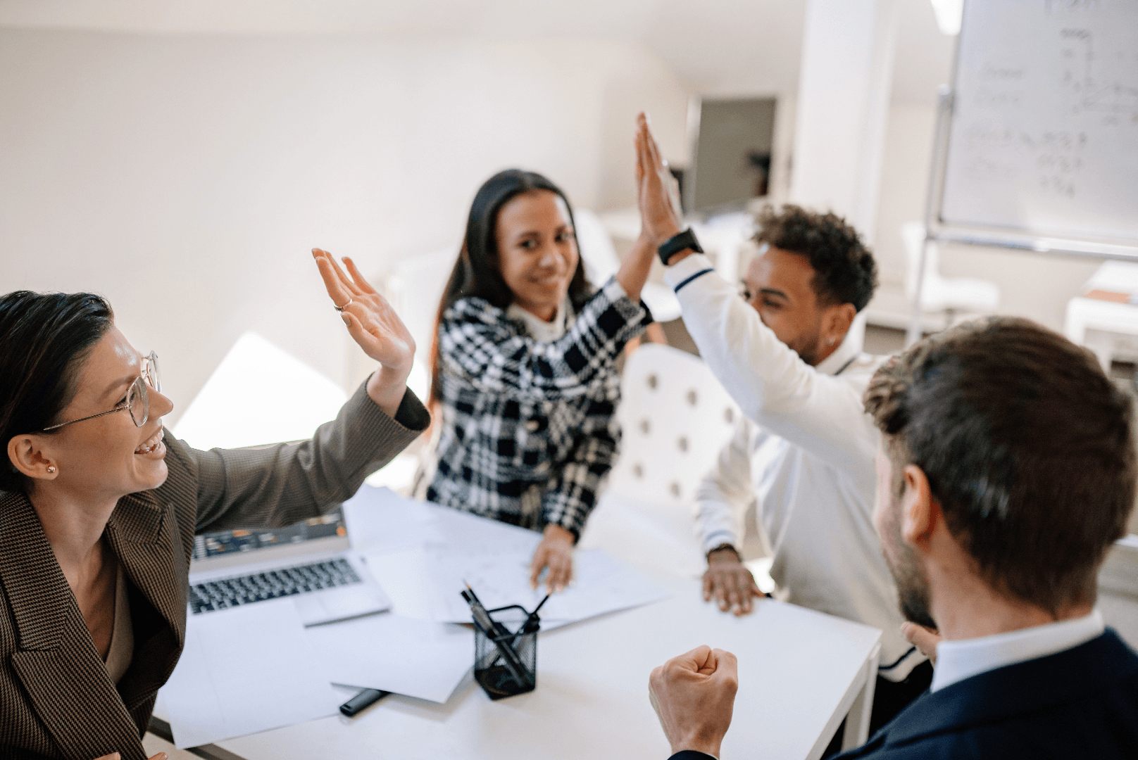 Four coworkers sitting at a desk high-fiving each other