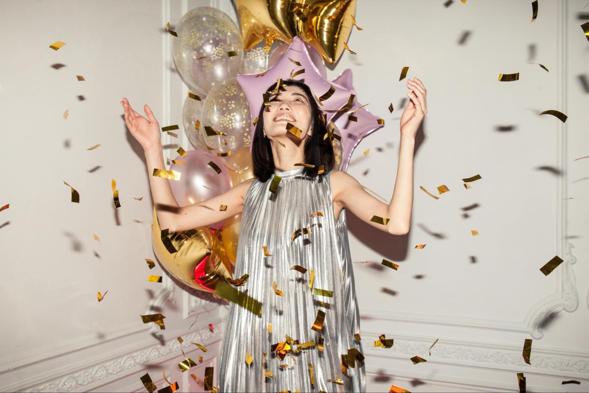 A woman looking entertained with confetti flying around and balloons behind her