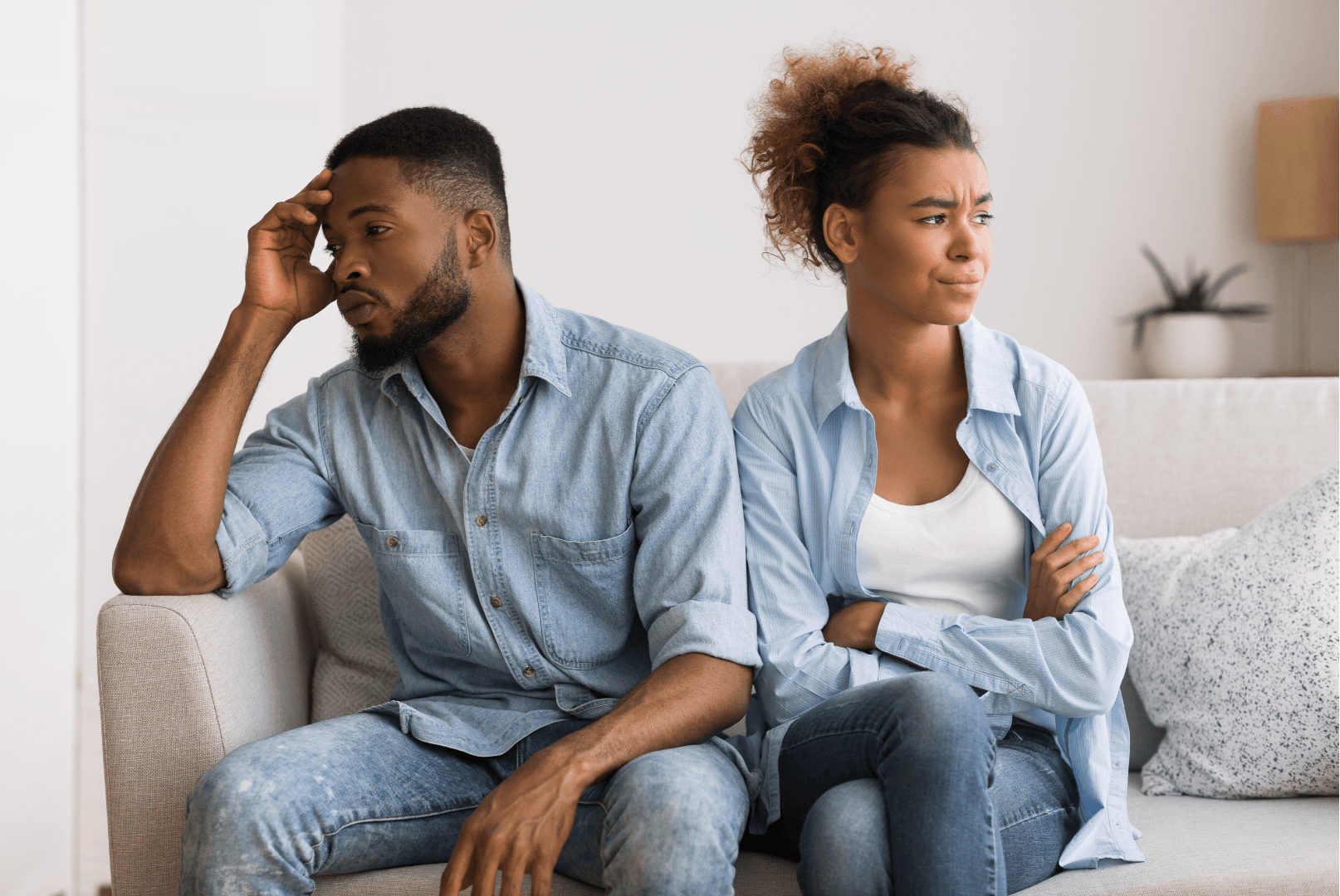 A man and a woman sit apart on a couch, their body language suggesting frustration or anger toward each other