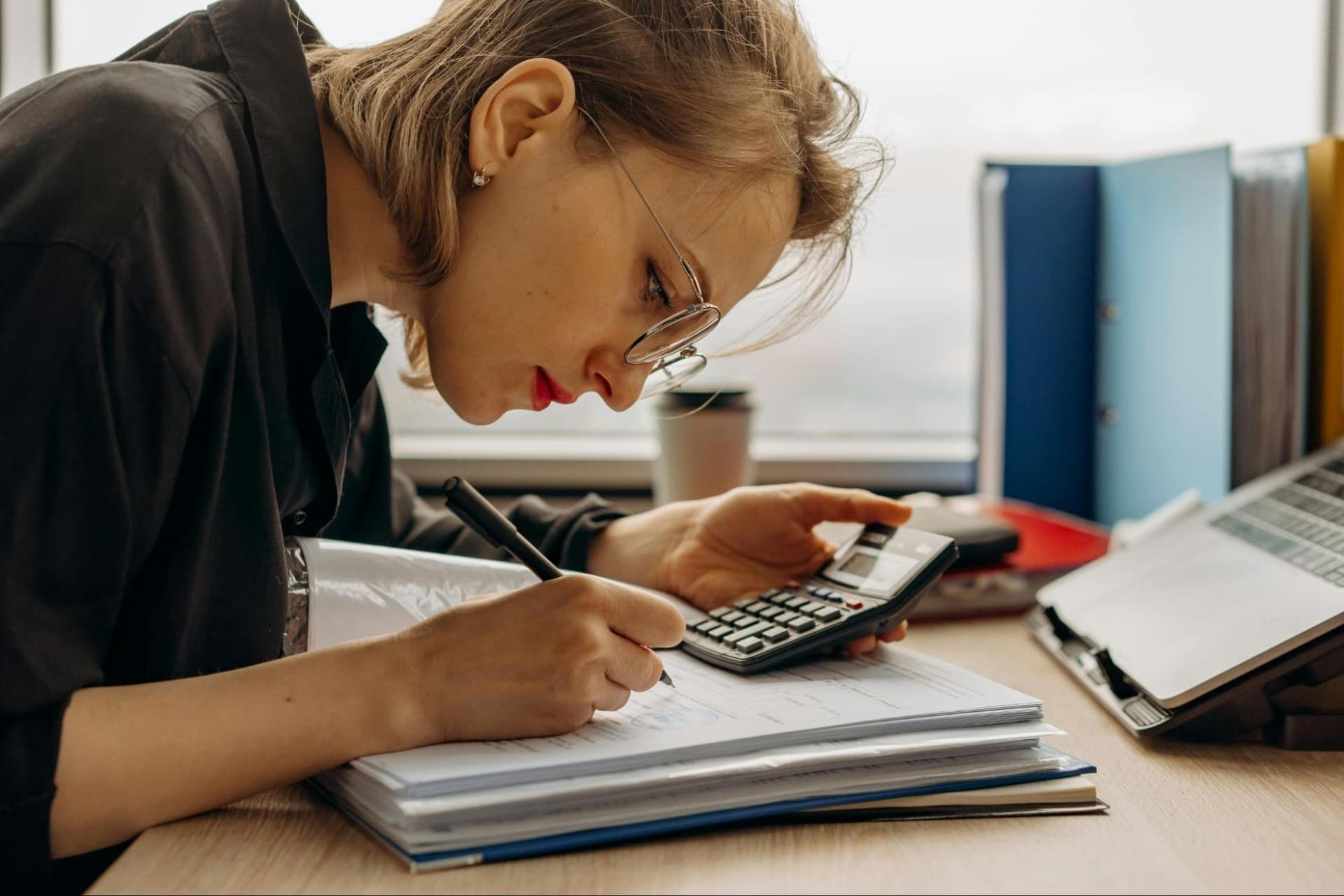 A woman using a calculator and writing in a notebook