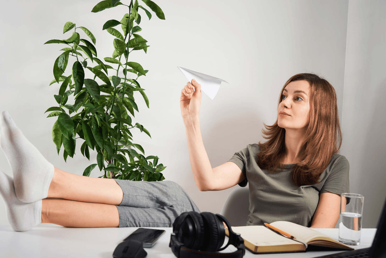 A woman with her legs raised on a desk throwing a paper airplane