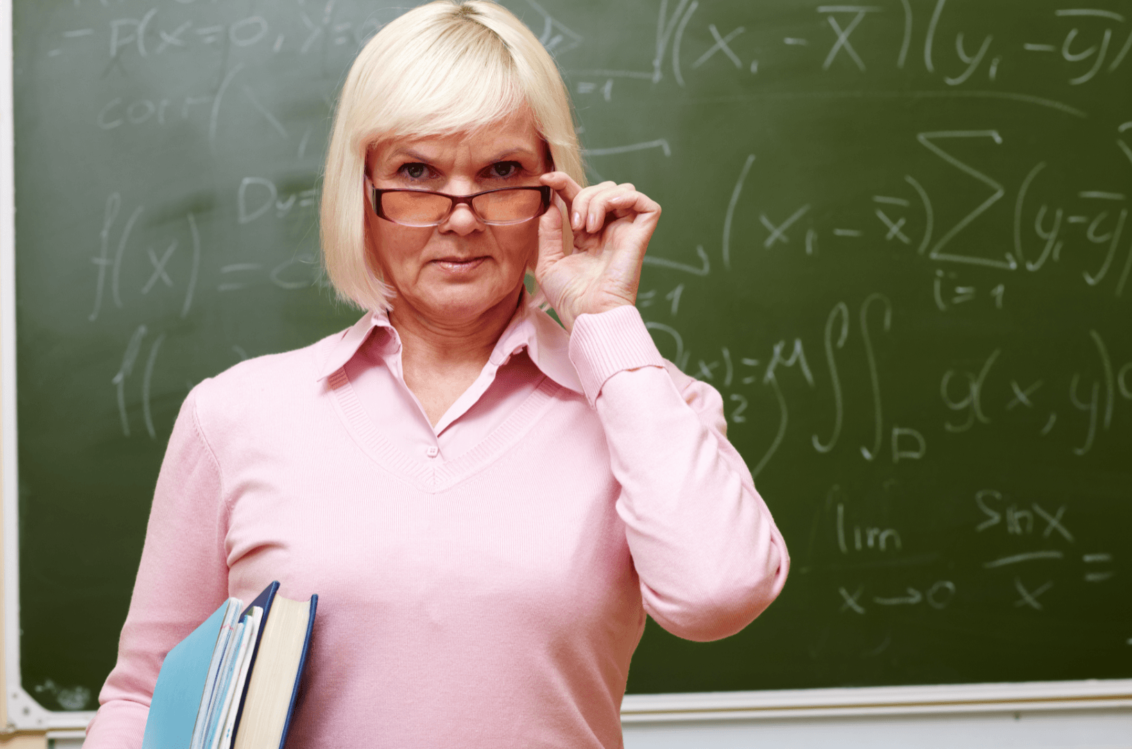A school teacher faces the camera while standing in front of a blackboard