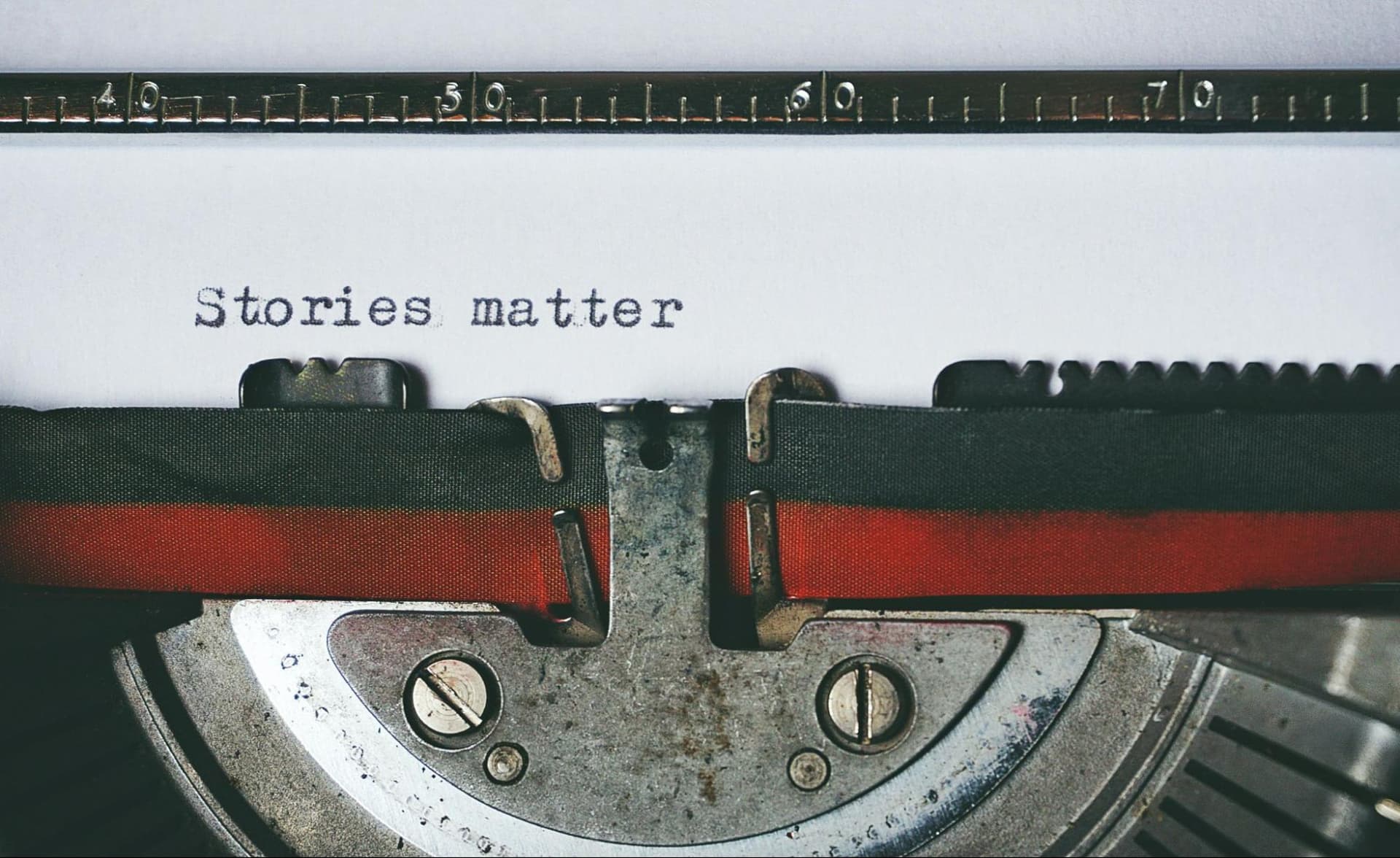 A sheet of paper in a typewriter with the words “stories matter” typed on it, shown in close-up