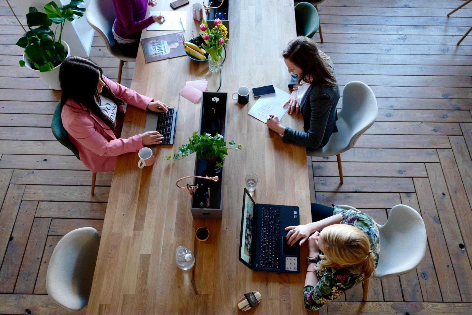 Top-down view of three women sitting side by side at a desk, each working on a laptop