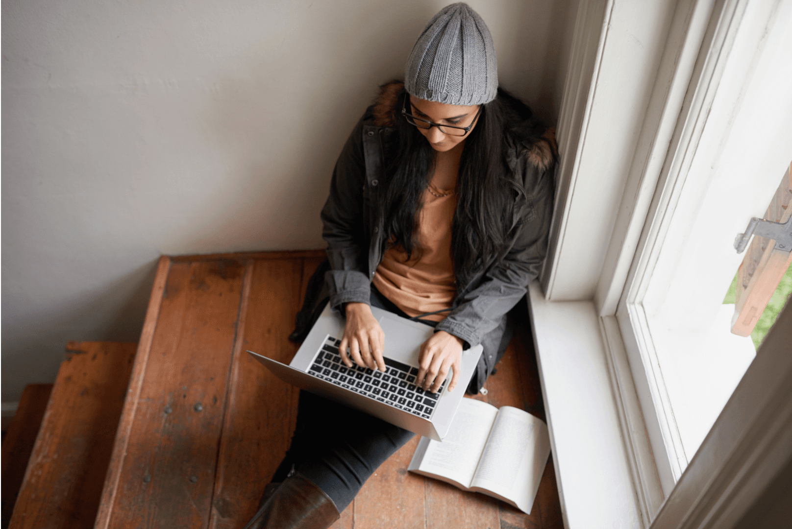 A young woman sitting on stairs working on a laptop with a notebook beside her