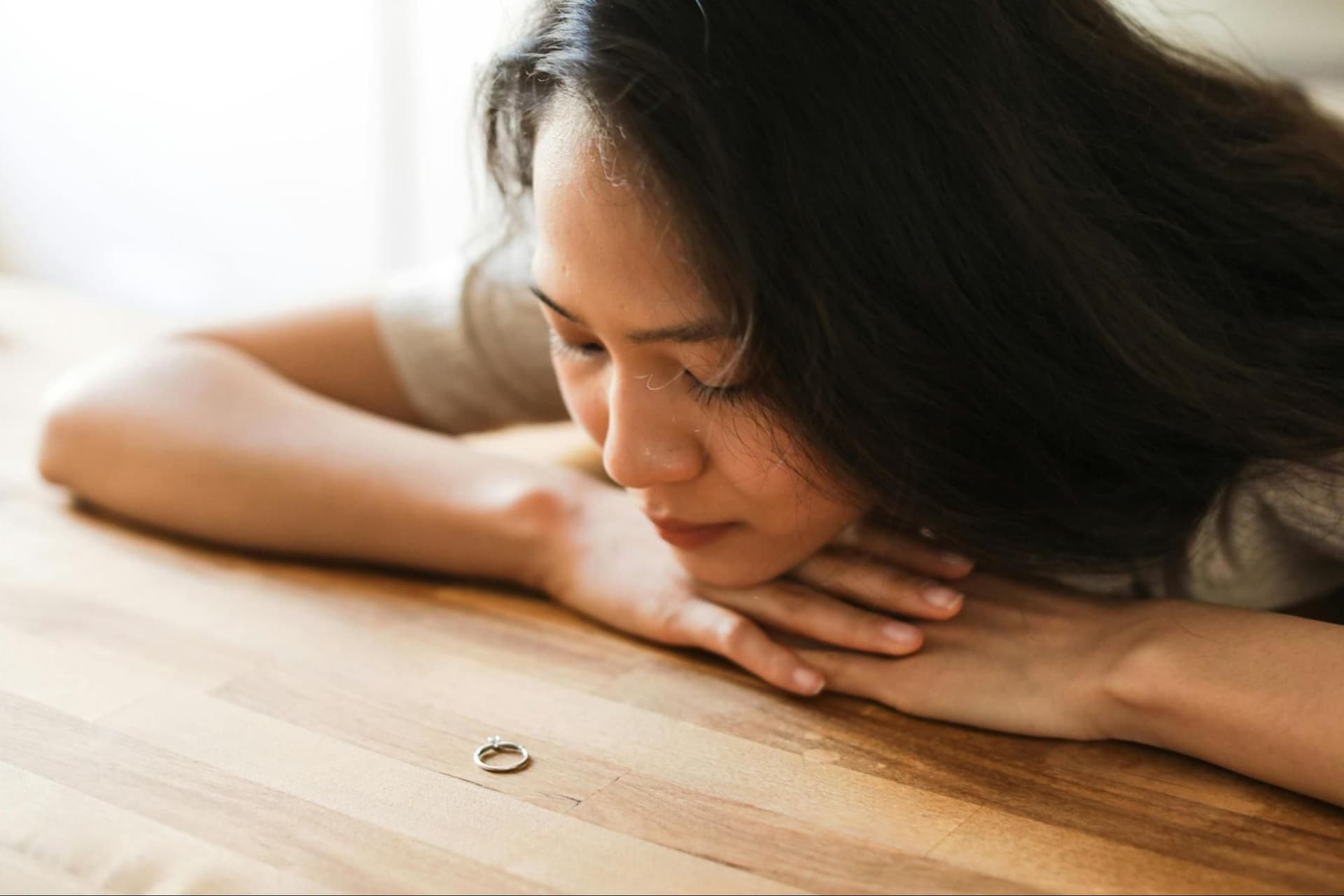 A woman sits at a table and looks at a ring placed in front of her