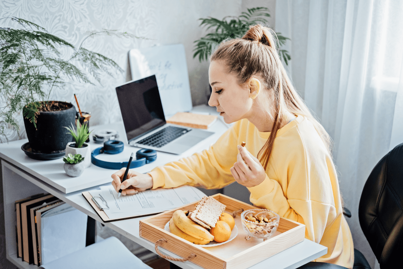 woman sitting at a desk, filling out a document and eating snacks
