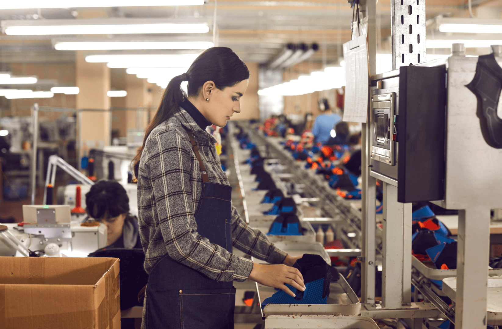 A woman wearing safety gear works on a factory assembly line, handling materials