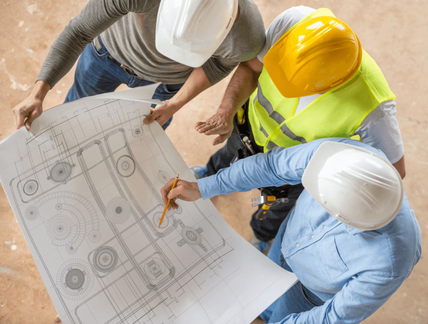 Three engineers in safety helmets examining a blueprint at a worksite