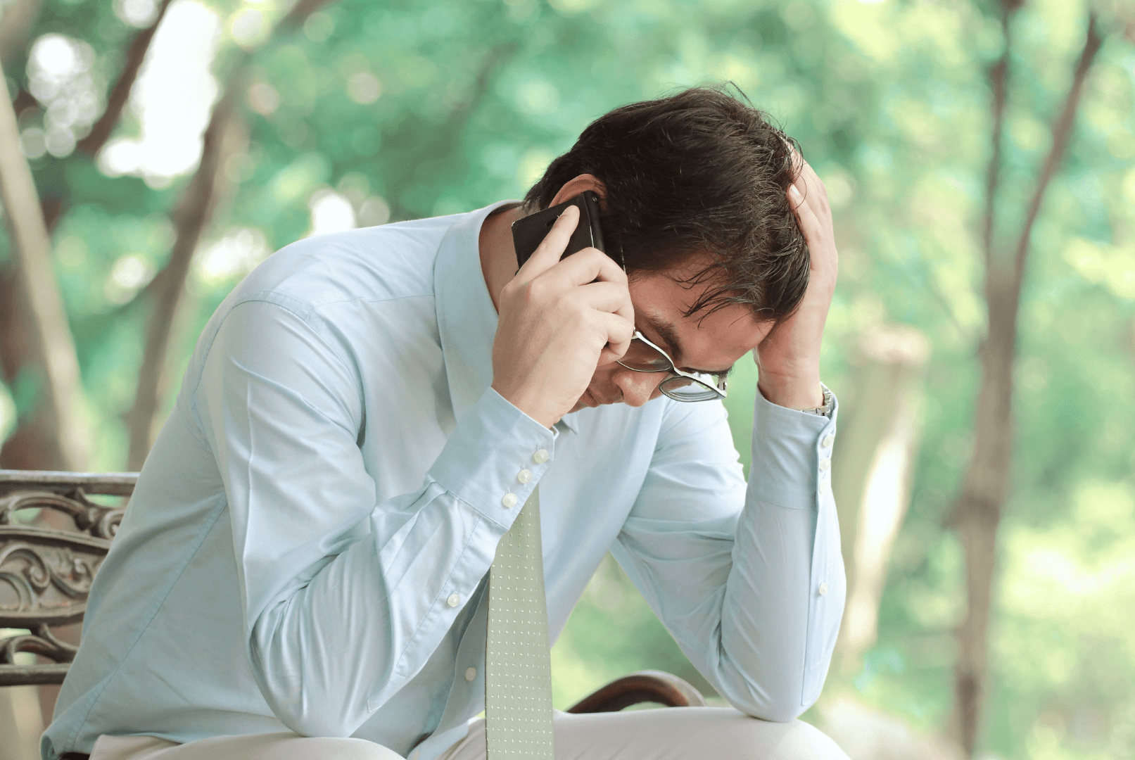 A man speaks on the phone while holding his head in one hand, appearing stressed or concerned