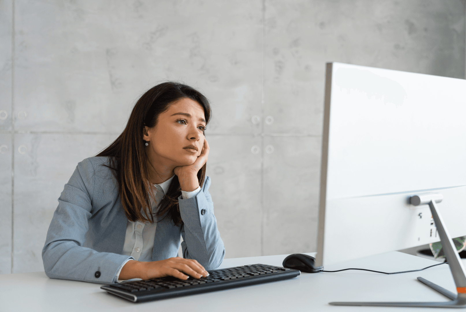 A woman sitting at a desk, working on a computer with her head resting in her hand