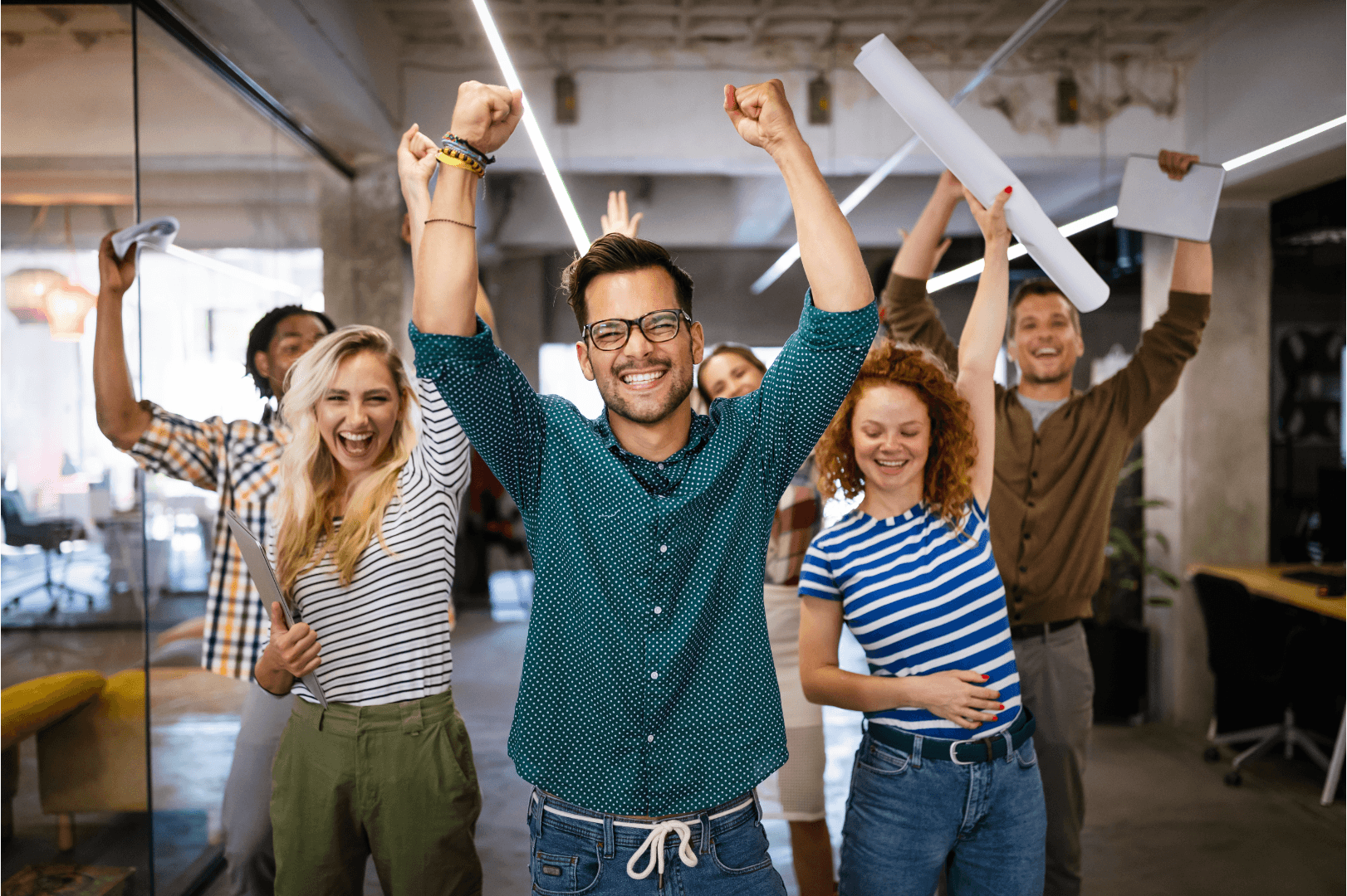Six smiling coworkers at a workplace raise their hands in celebration or excitement