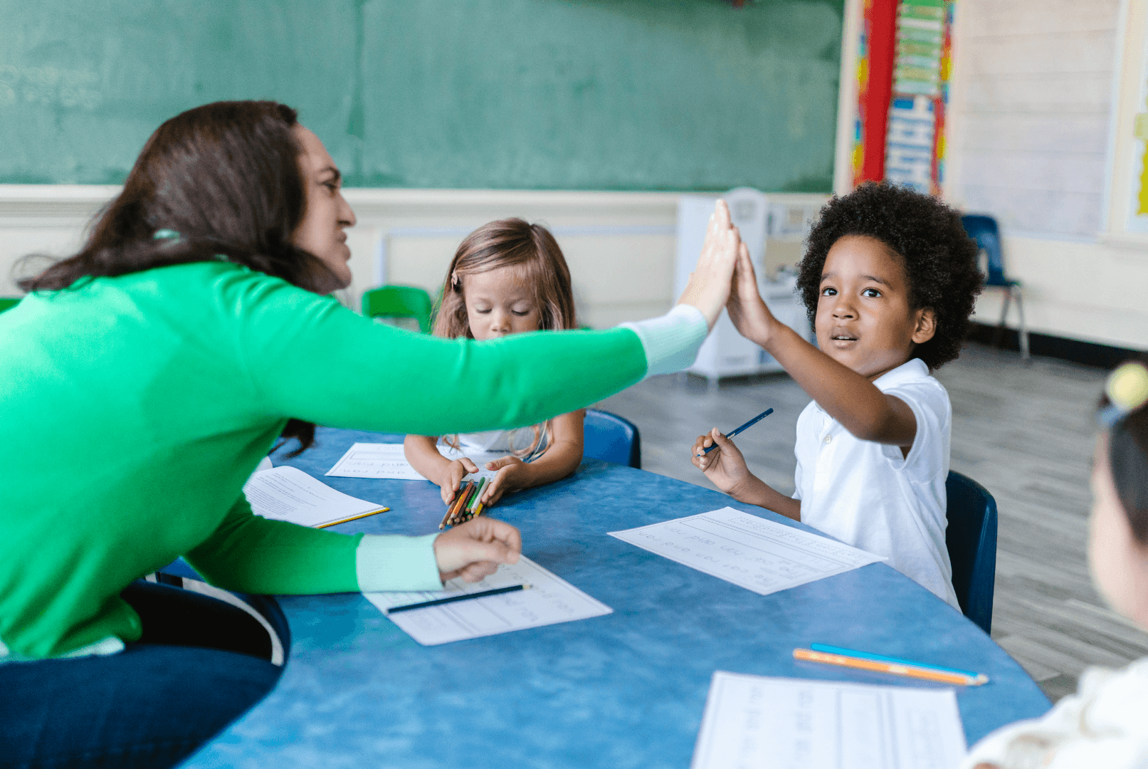 A preschool teacher high-fiving a boy with other children in the background