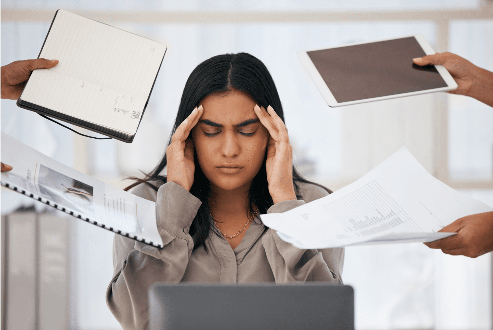 A woman holds her head in frustration as several hands pass her documents, showing workplace stress and overwhelm