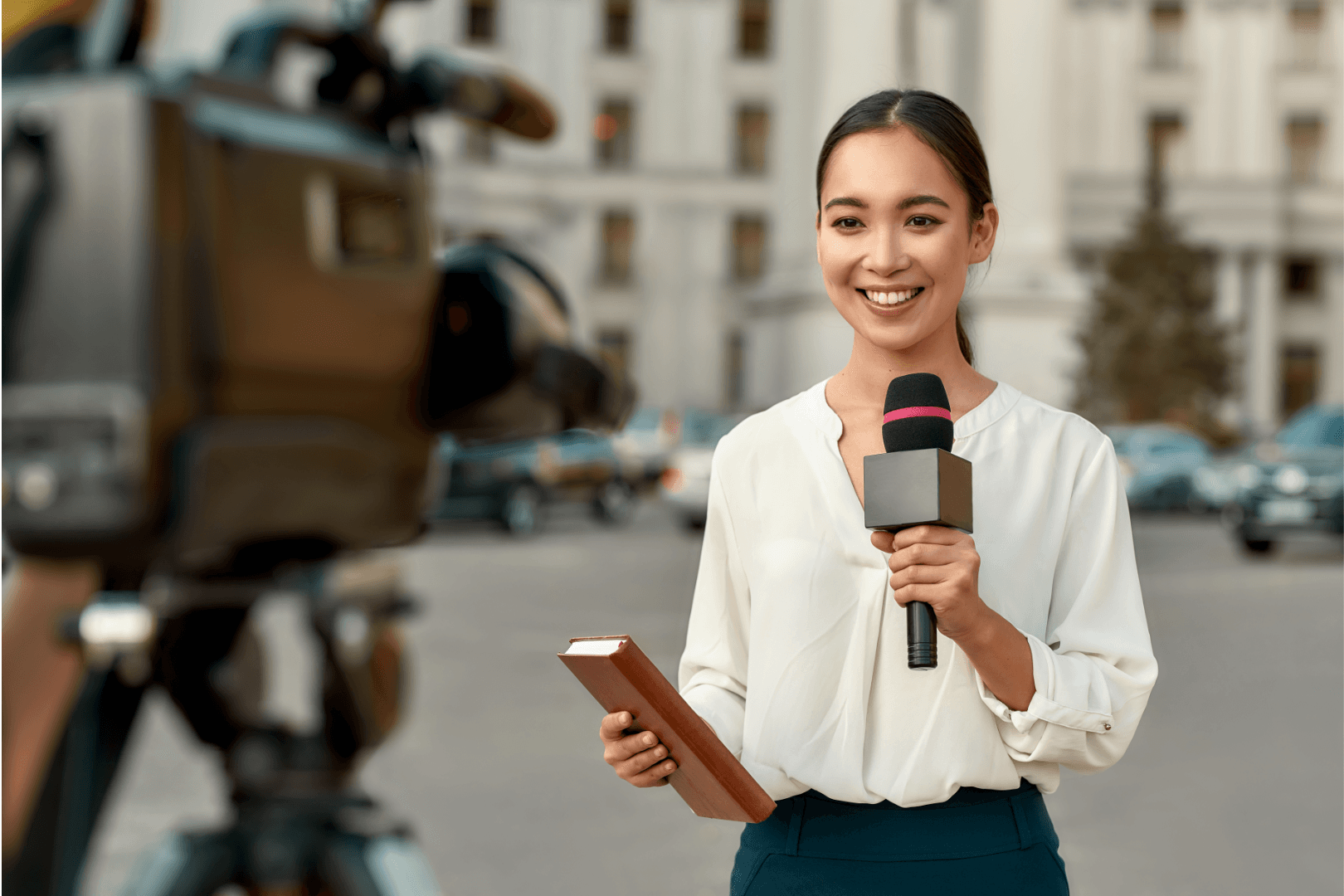 A journalist holding a notebook and microphone speaking in front of a camera
