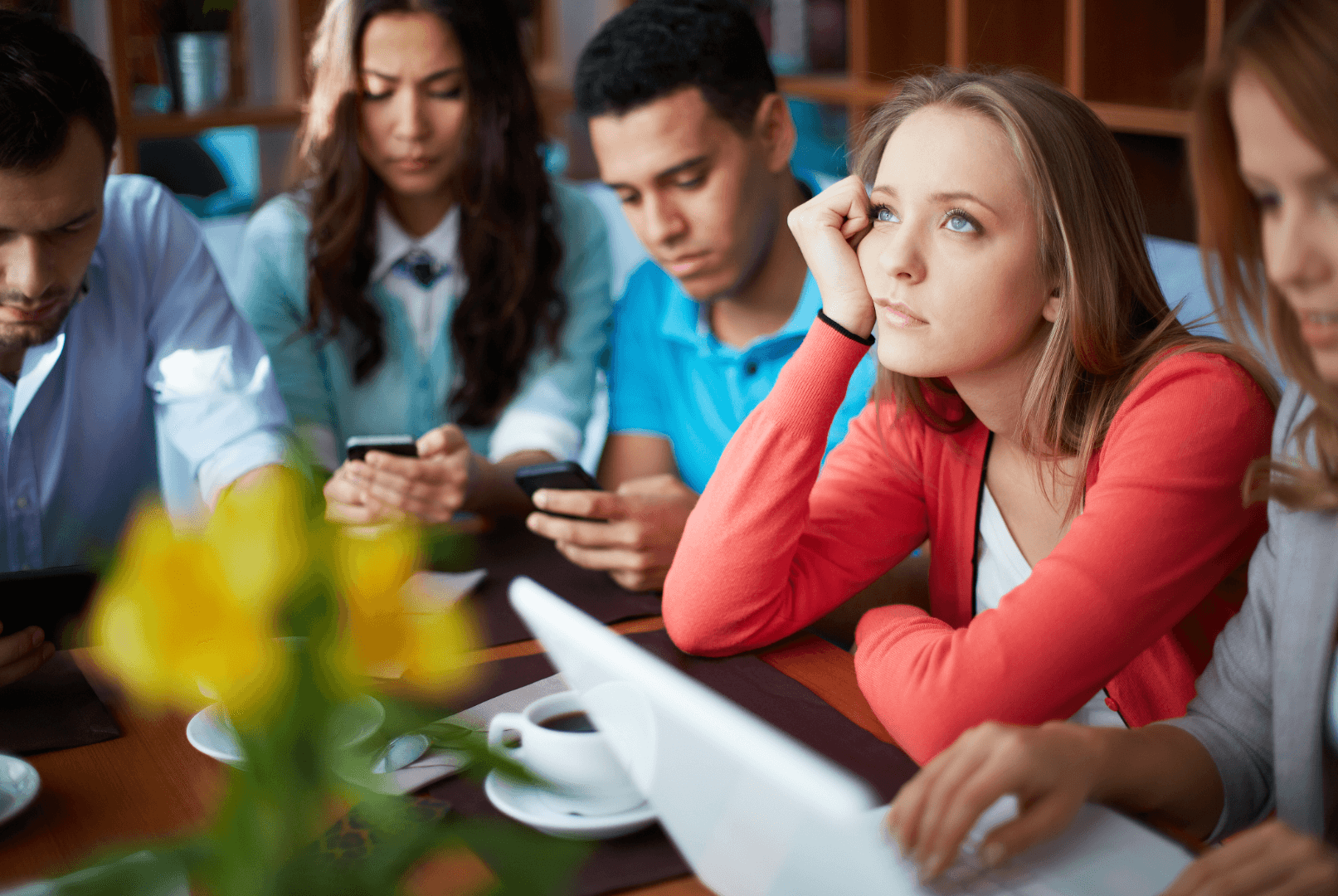 A group of five people sit around a desk in discussion, with the camera focusing on a woman deep in thought