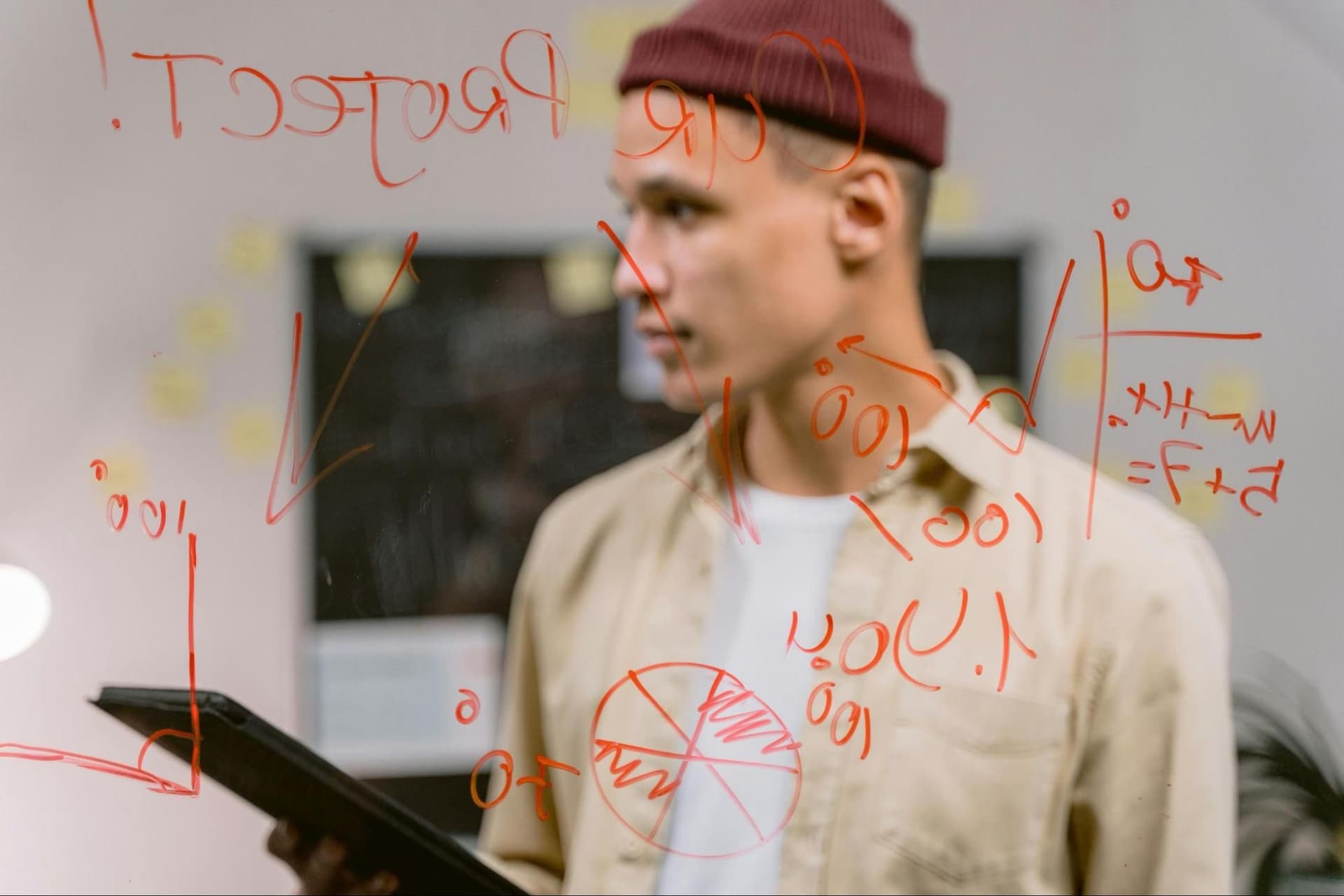 A young man standing behing a see-through whiteboard
