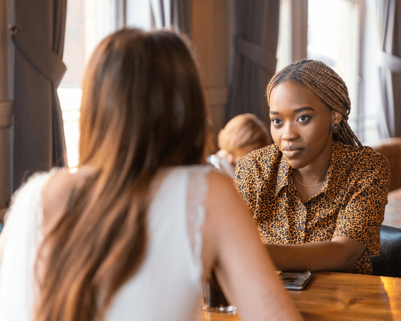 Two women sitting at a table, one looking at the other who is turned away from the camera