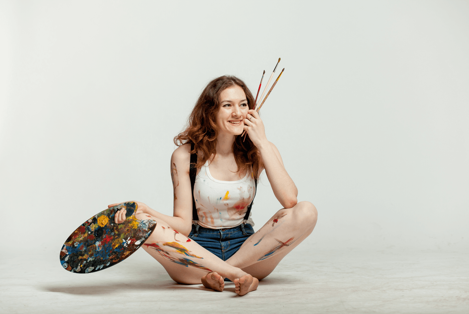 A woman sitting on the floor holding a paintbrush and a palette