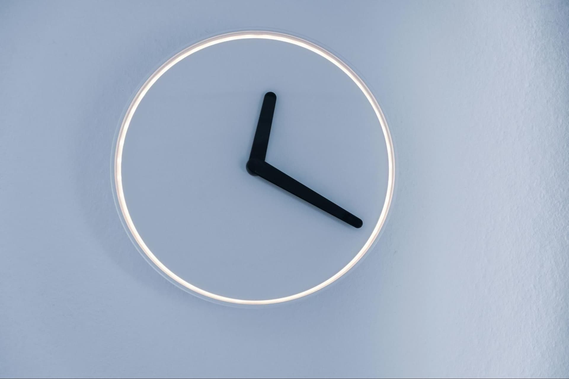 Minimalist wall clock without numbers, showing only two hands on a light blue background