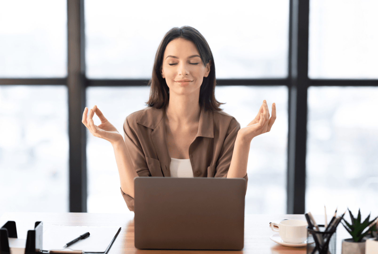 A woman meditating while sitting at a table with a laptop in front of her