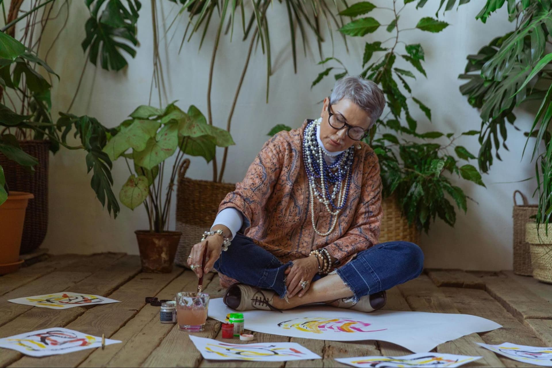 A woman sitting on the floor and painting, with multiple papers in front of her